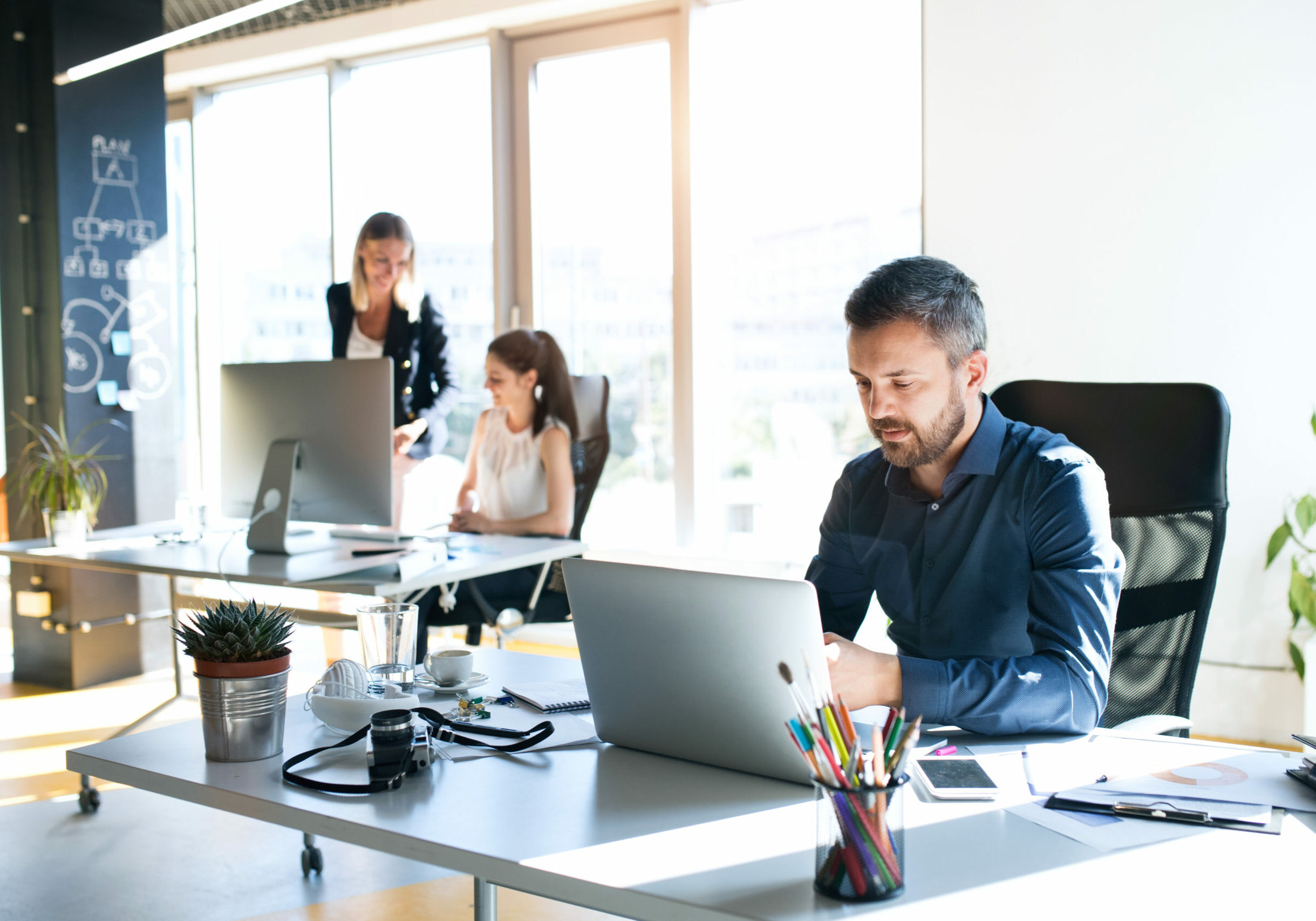 Three business people in the workplace. Two women and man sitting in the office working together.